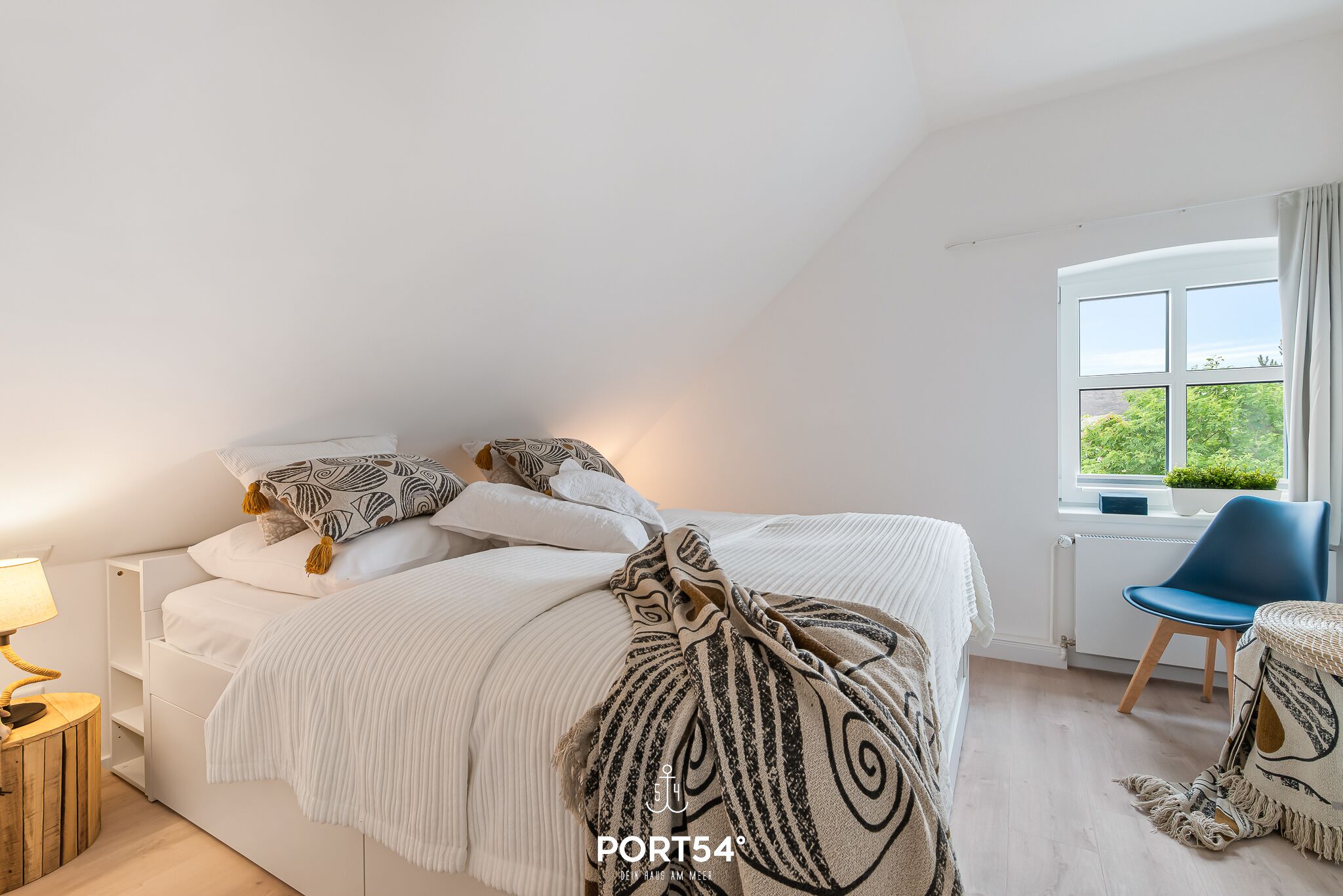 Une chambre à coucher avec un lit, une chaise, une lampe et une fenêtre donnant sur un beau paysage.