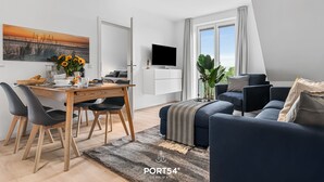 Ein modernes Wohnzimmer mit Essbereich, einem Flachbildfernseher und einem großen Fenster mit Vorhängen.