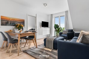 A modern living room with a dining area, a flat-screen TV, and a large window with curtains. - Hohe Wacht – for 6 people, rural, idyllic, North Sea (Emmelsbüll)