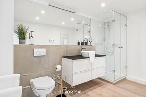 Un baño moderno con inodoro, lavabo y ducha con mampara de vidrio.