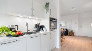 A modern kitchen with white cabinets, stainless steel appliances, and a wooden dining area. - Hohe Wacht – for 6 people, rural, idyllic, North Sea (Emmelsbüll)