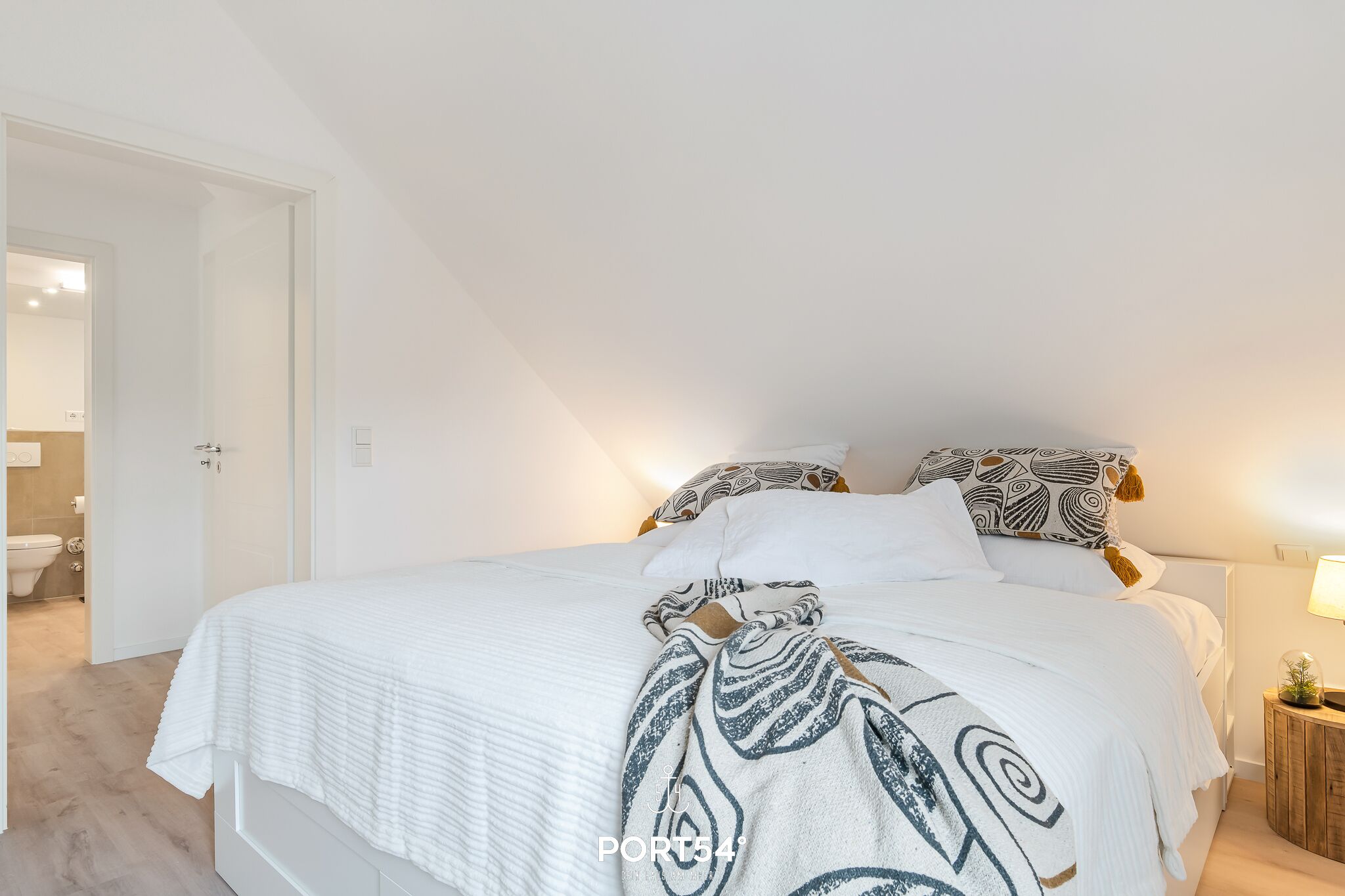 Une chambre à coucher avec un lit, des oreillers, une table de chevet et une lampe.