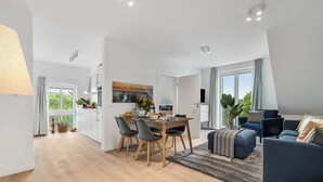 Ein modernes Wohnzimmer mit einem dunkelblauen Sofa, einem Holzespeisetisch mit Stühlen und einem großen Fenster mit Vorhängen.