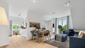 A modern living room with a dark blue sofa, a wooden dining table with chairs, and a large window with curtains. - Hohe Wacht – for 6 people, rural, idyllic, North Sea (Emmelsbüll)