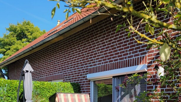 Une maison en briques avec un patio, du mobilier d’extérieur et un espace salon abrité.