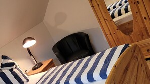 Une chambre à coucher avec un cadre de lit en bois, un fauteuil en cuir noir, une table de chevet avec une lampe et un coussin à rayures.