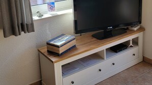 Une pièce avec un téléviseur posé sur un meuble en bois, une fenêtre avec des rideaux et une petite figurine sur le rebord de la fenêtre.