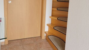 Une porte en bois avec un trou de serrure, un sol carrelé et un escalier en colimaçon agrémenté d’une étagère noire fixée au mur.