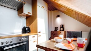 A modern kitchen with a built-in oven, wooden cabinets, and a dining table set for breakfast. - Hummerklippen Ferienwohnungen (Helgoland)