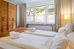 Ein Hotelzimmer mit Holzschrank, Bett mit weißer Bettwäsche, Vorhängen am Fenster und einer Nachttischlampe.