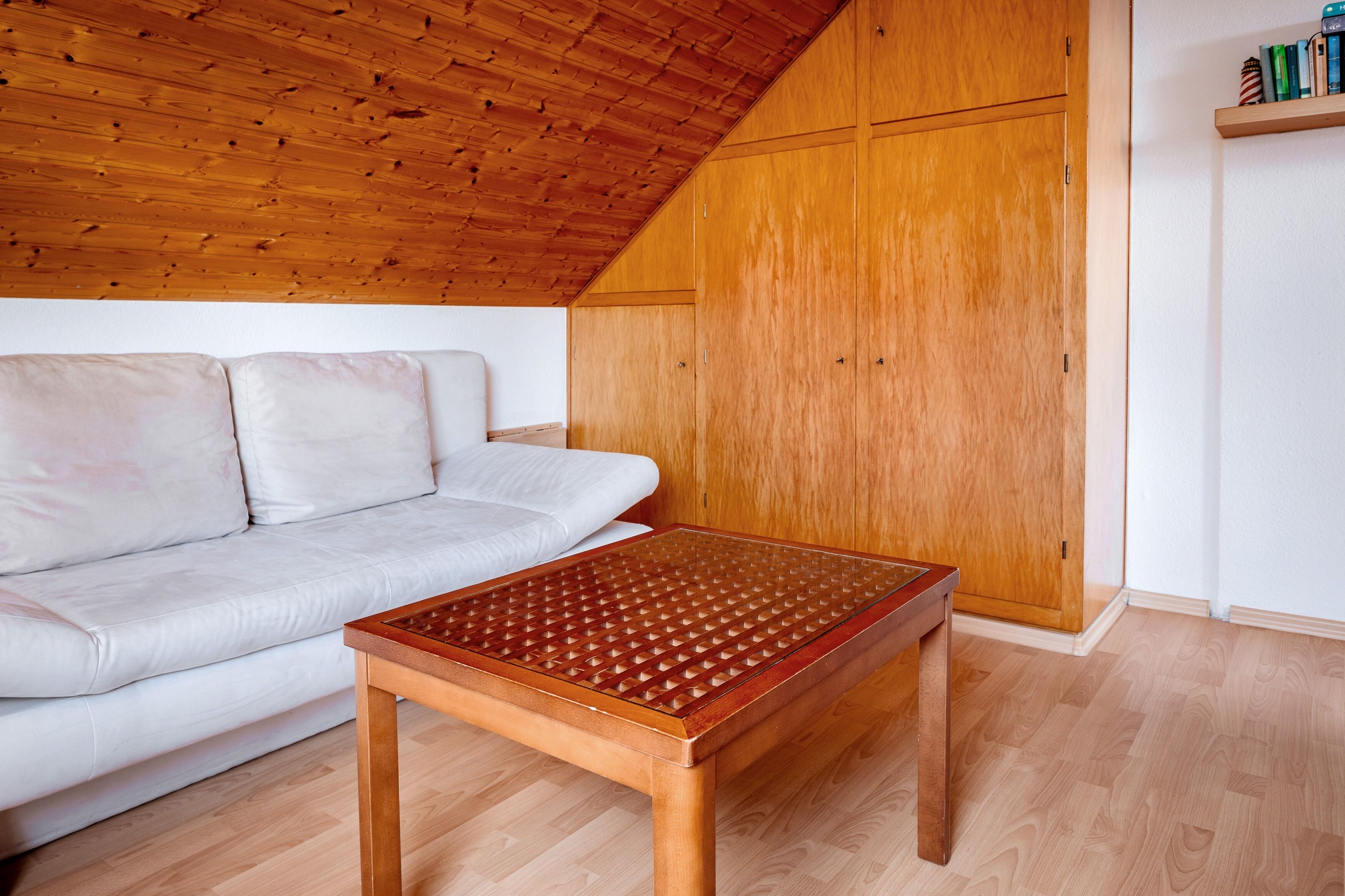 Una habitación con techo de madera, un sofá blanco, una mesa de madera y un armario de madera.
