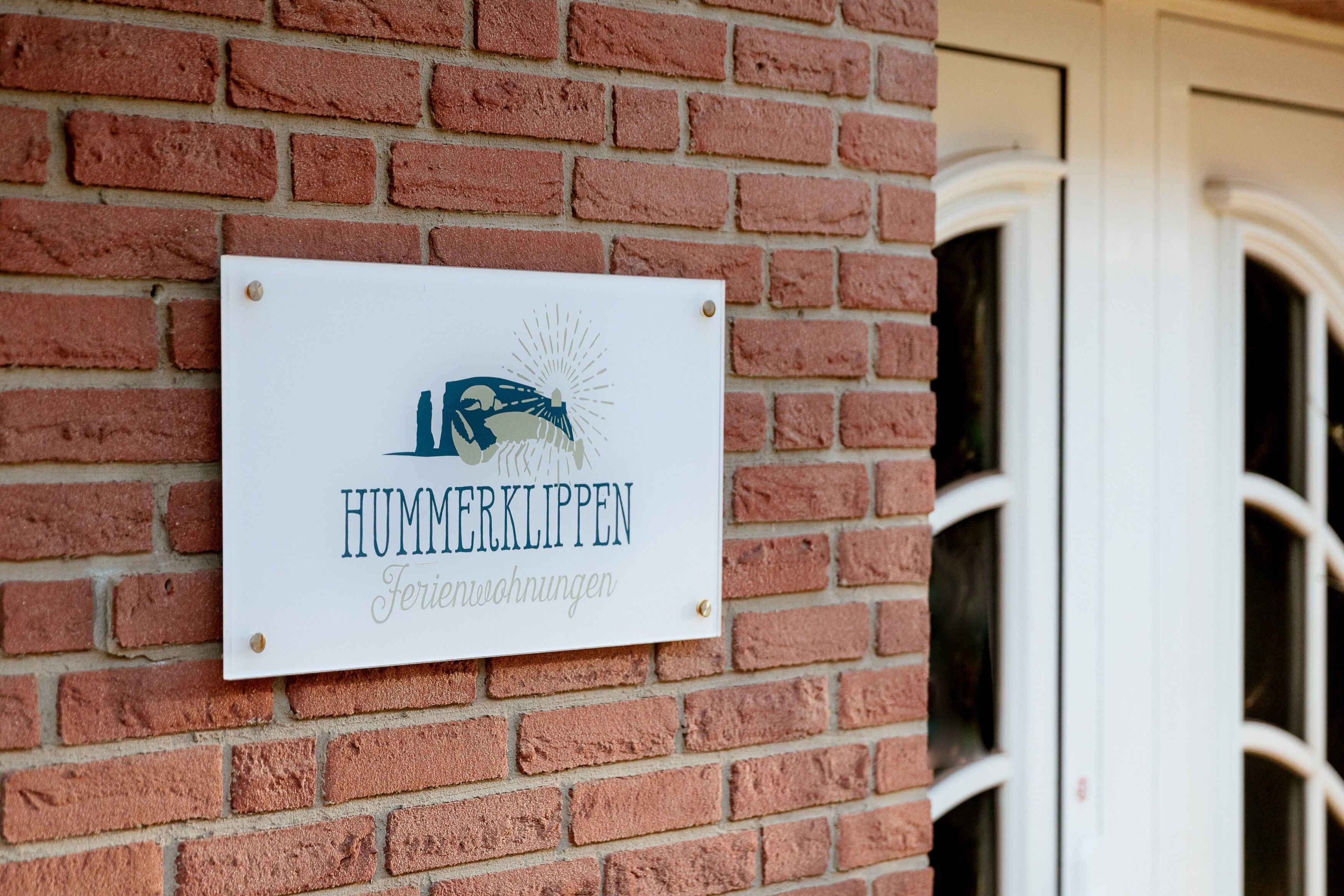 Une enseigne sur un mur de briques, portant l’inscription « HUMMERKLIPPEN Ferienwohnungen » et un logo.