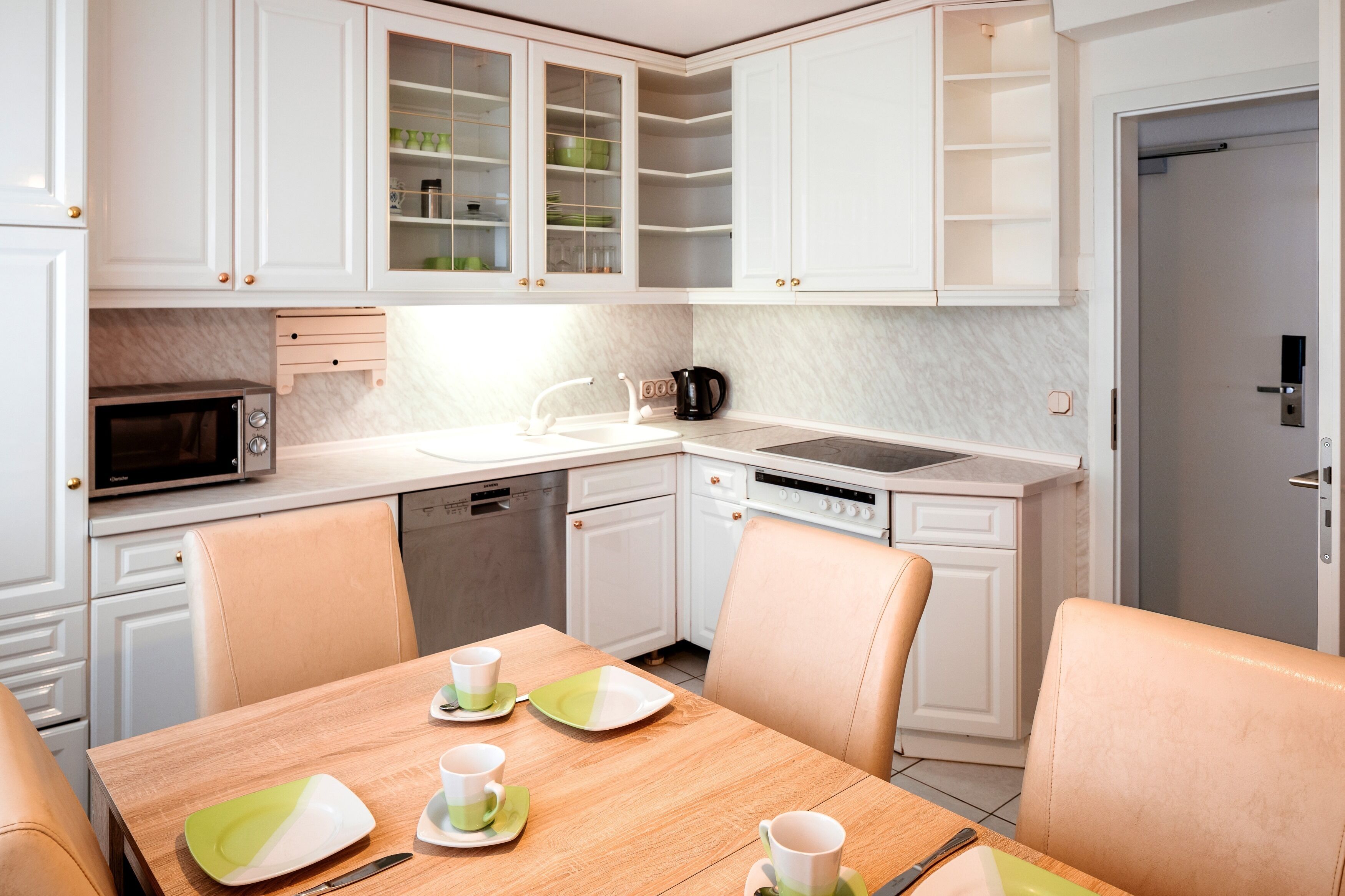Une cuisine moderne avec des meubles blancs, un four à micro-ondes, une machine à café et un coin repas avec une table mise pour deux personnes.