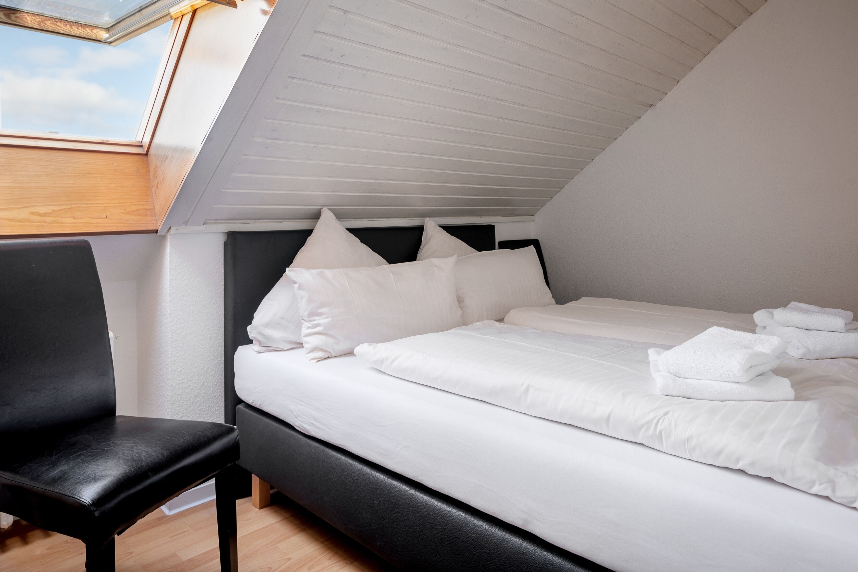 A bedroom with a bed, a chair, and a skylight.