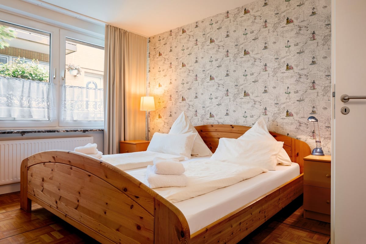 Ein ordentlich bezogenes Bett mit weißen Leinen und Kissen, eine Nachttischlampe und ein Holz-Kopfteil.