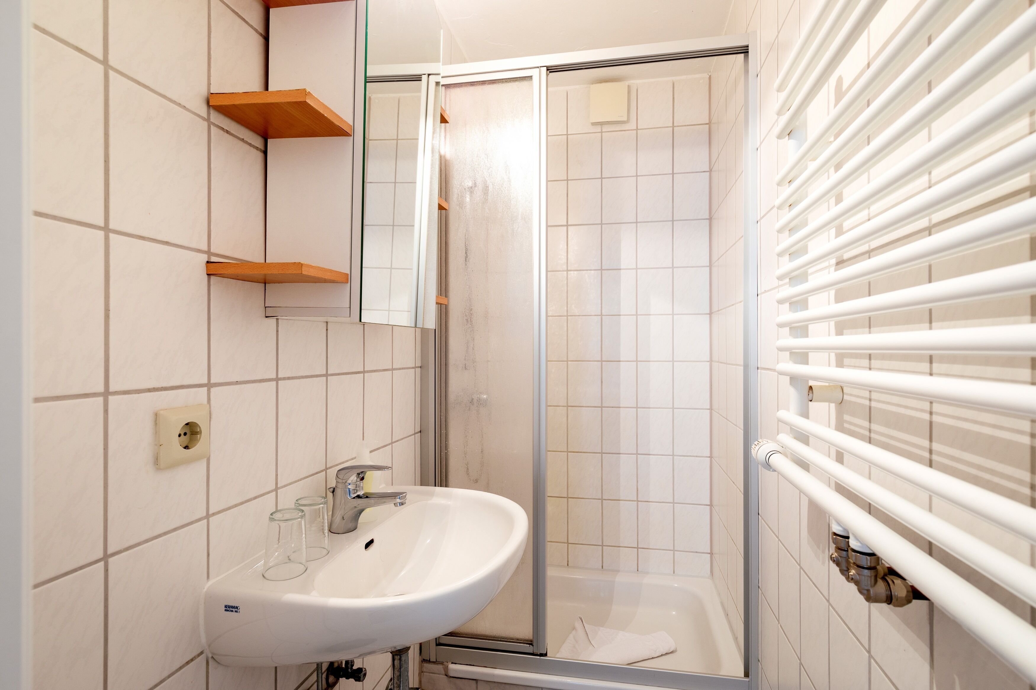 Un baño con lavamanos blanco, espejo y cabina de ducha de vidrio.