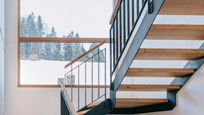 A modern staircase with wooden steps and metal railings, leading to a room with a large window offering a view of a snowy landscape. - Baldauf Apartment - Apartment (Hittisau)