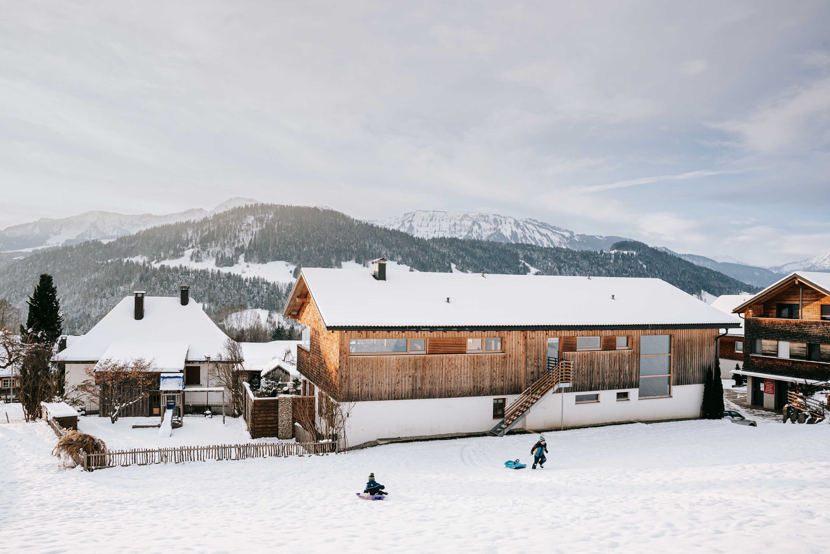 Eine Holzhütte mit schneebedecktem Dach, einer Holzdiele und einer Skipiste im Hintergrund.