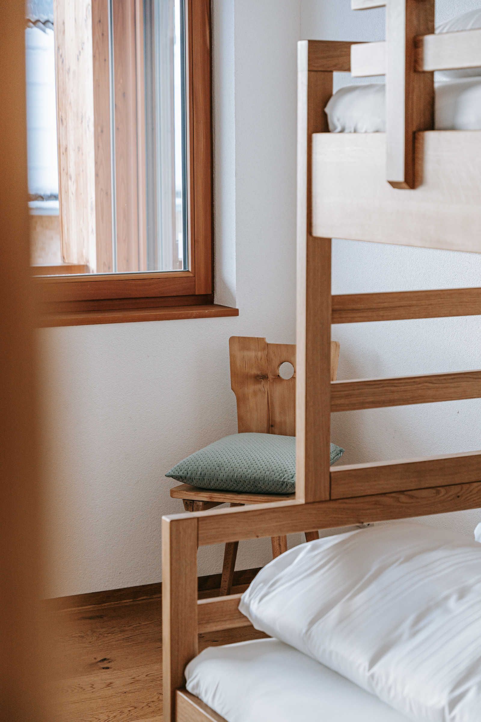 A bunk bed with a wooden headboard and a single bed below. A window with wooden blinds is visible in the background.