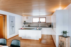 Une cuisine moderne avec un plafond en bois, des armoires blanches, un îlot central et une grande fenêtre.
