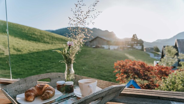 A tray with croissants, coffee, and a vase of flowers on a table with a scenic view. - Baldauf Apartment - Apartment (Hittisau)