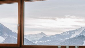 A hotel room with a large window offering a view of snow-covered mountains. - Baldauf Apartment - Apartment (Hittisau)