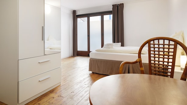 A hotel room with a bed, a wooden chair, a table, and a wardrobe. - Haus Hoog Stean (Helgoland)
