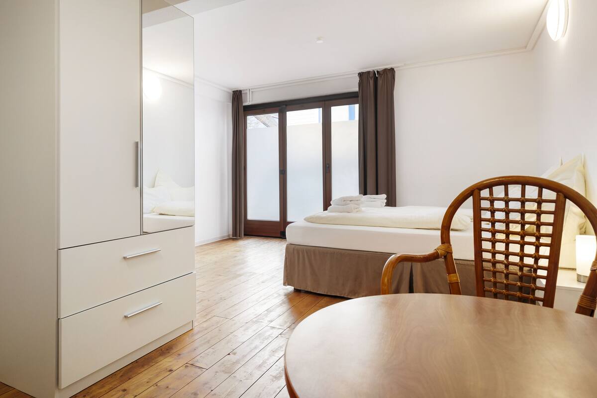 Una habitación de hotel con una cama, una silla de madera, una mesa y un armario.