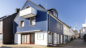 A two-story building with a blue exterior, a balcony on the upper floor, and a sign on the ground floor. - Haus Hoog Stean (Helgoland)
