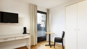 A room with a TV mounted on the wall, a desk with drawers, a chair, and a wardrobe. - Haus Hoog Stean (Helgoland)