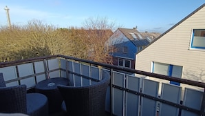 A balcony with wicker furniture and a railing, overlooking a residential area with houses and a power line. - Haus Hoog Stean (Helgoland)