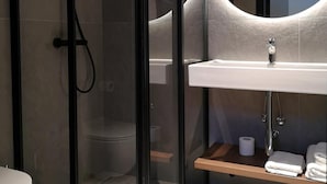 A modern bathroom with a glass-enclosed shower, a white sink, and a mirror with a circular frame. - Polonezas (Vilnius)