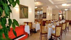 A dining area with tables set for service, a piano, and a large painting on the wall. - Polonezas (Vilnius)