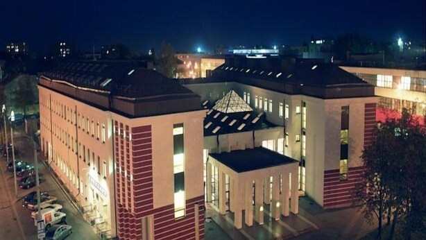 A modern building with a central atrium, multiple windows, and a parking area in front. - Polonezas (Vilnius)