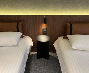 Ein Hotelzimmer mit zwei Betten, einem kleinen runden Tisch und einer an der Wand montierten Steuerung.