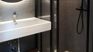 A modern bathroom with a glass-enclosed shower, a white sink, and a large mirror. - Polonezas (Vilnius)