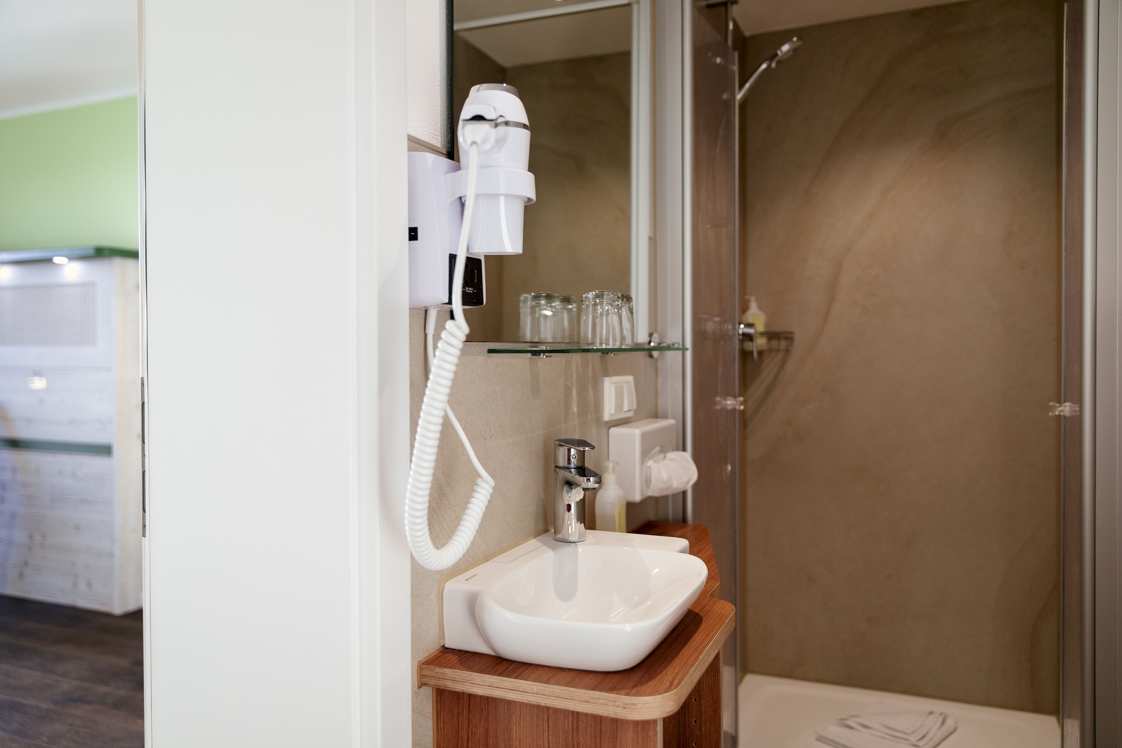 A bathroom with a white sink, a hairdryer, and a glass shower enclosure.