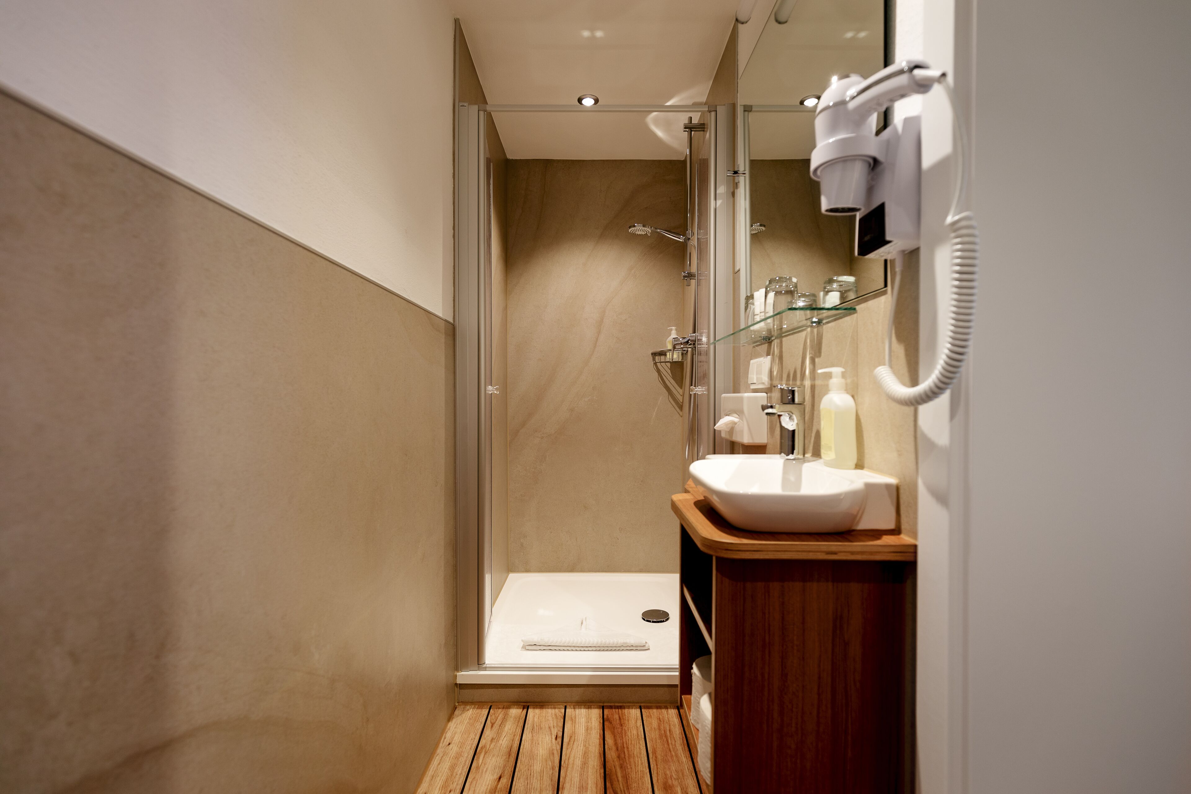 A modern bathroom with a glass shower enclosure, a wooden vanity, and a white sink.