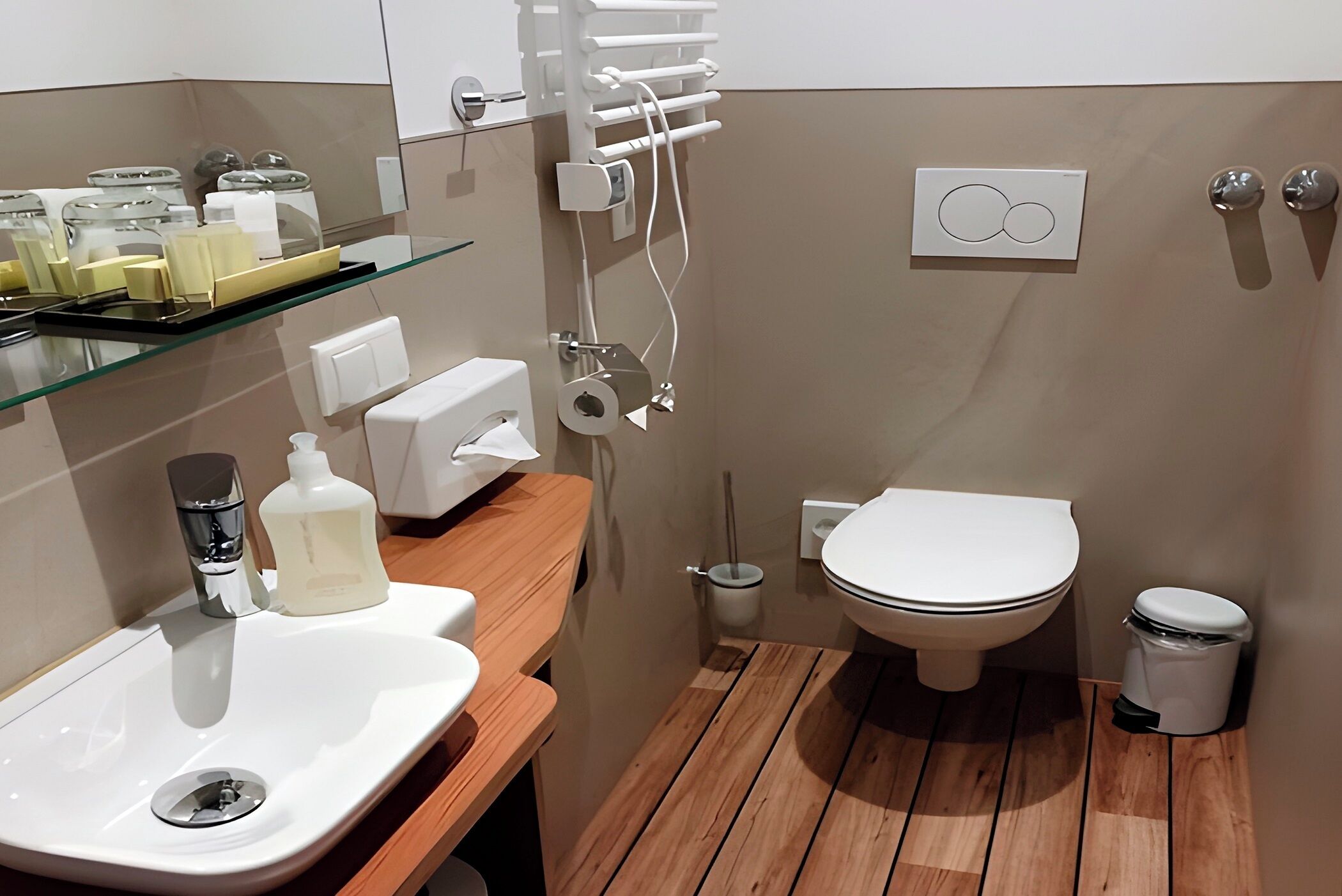 A modern bathroom with a wooden vanity, a white sink, a toilet, and a glass shelf with toiletries.