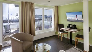 A hotel room with a large window, a glass table, two chairs, a coffee maker, and a television on the wall. - Insulaner Ferienwohnungen (Helgoland)
