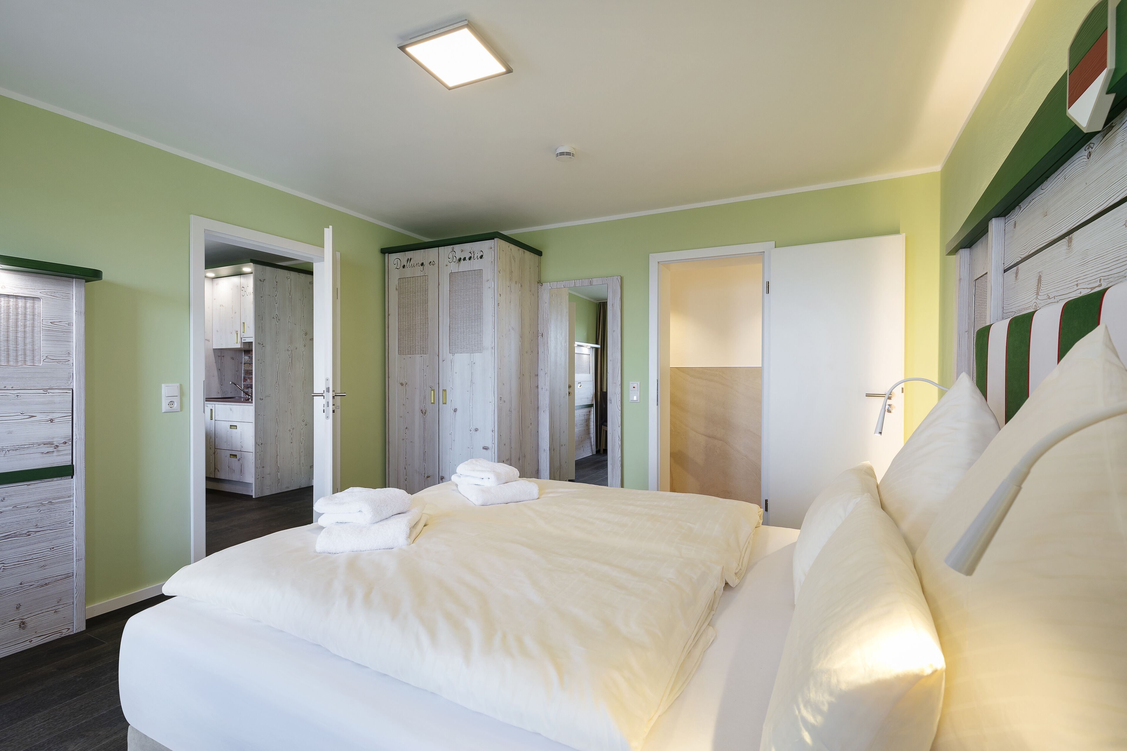 A hotel room with a large bed, a bathroom, and a kitchenette.