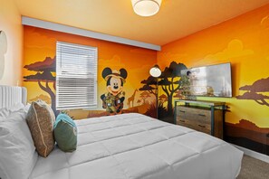 Een slaapkamer met een groot bed, een raam met zonwering, een muurschildering van Mickey Mouse en een dressoir met spiegel.