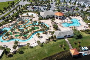 Oversigtsbillede af et resort med flere swimmingpools, en golfbane og en bro med både.