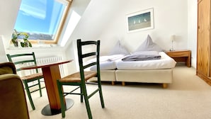 A cozy room with a bed, a desk, and a chair. There's a window with a view of the sky and a picture on the wall. - Haus Germania (Helgoland)