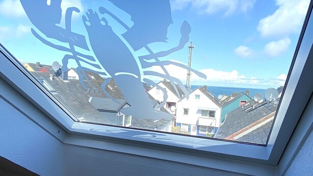 A skylight with a view of houses and a tower. - Haus Germania (Helgoland)