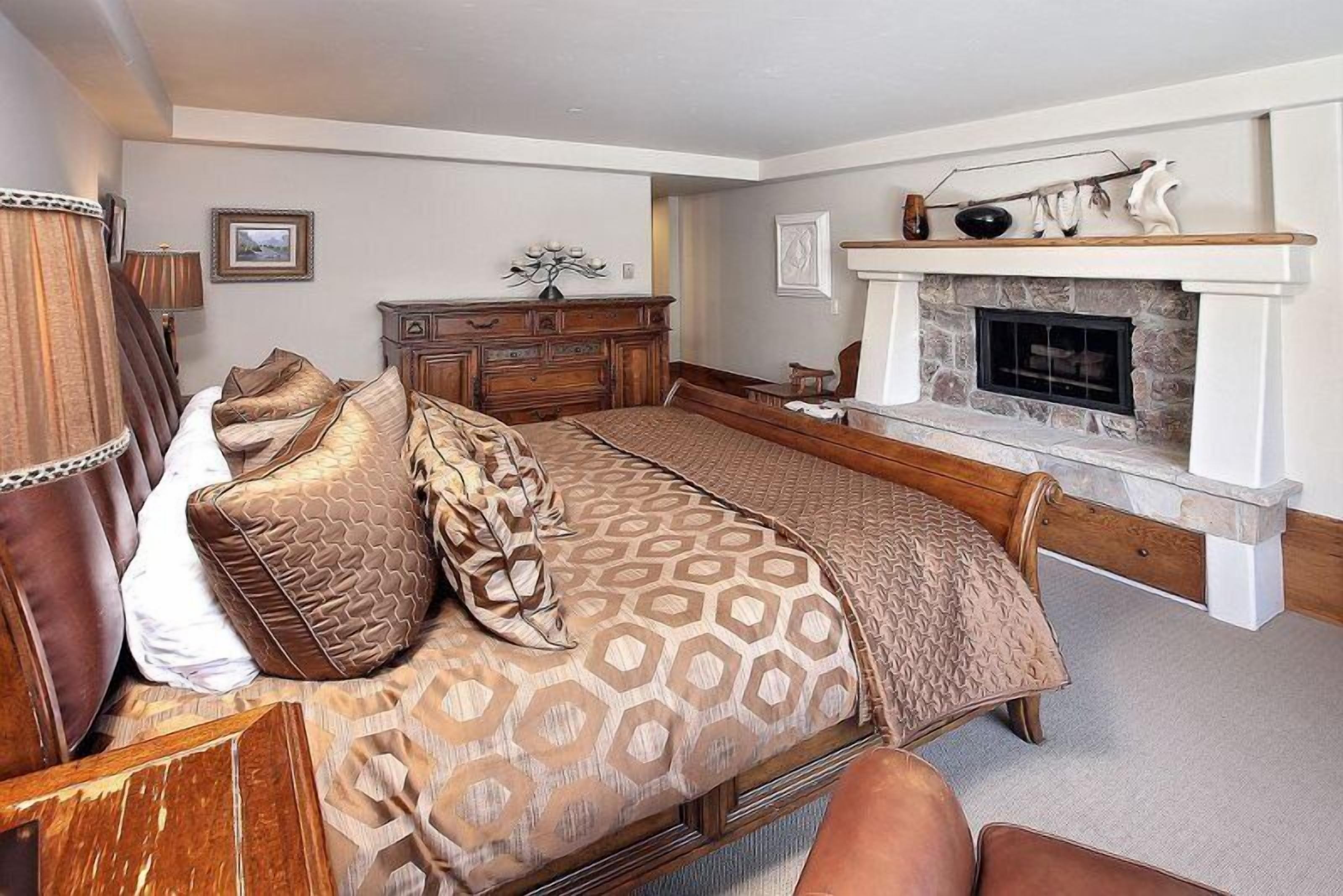 Ein Schlafzimmer mit einem großen Bett, einem hölzernen Schminktisch, einem Kamin und einem an der Wand befestigten Regal.