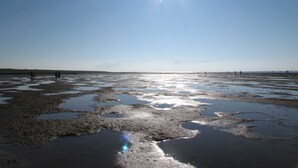 Een vlak, uitgestrekt landschap met een heldere lucht en een felle zon.