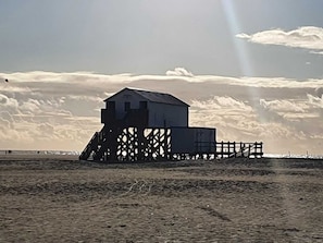 A beach house with a large deck and a small shed. - Rotes Atelierhaus, Deutschland (Nordstrand)