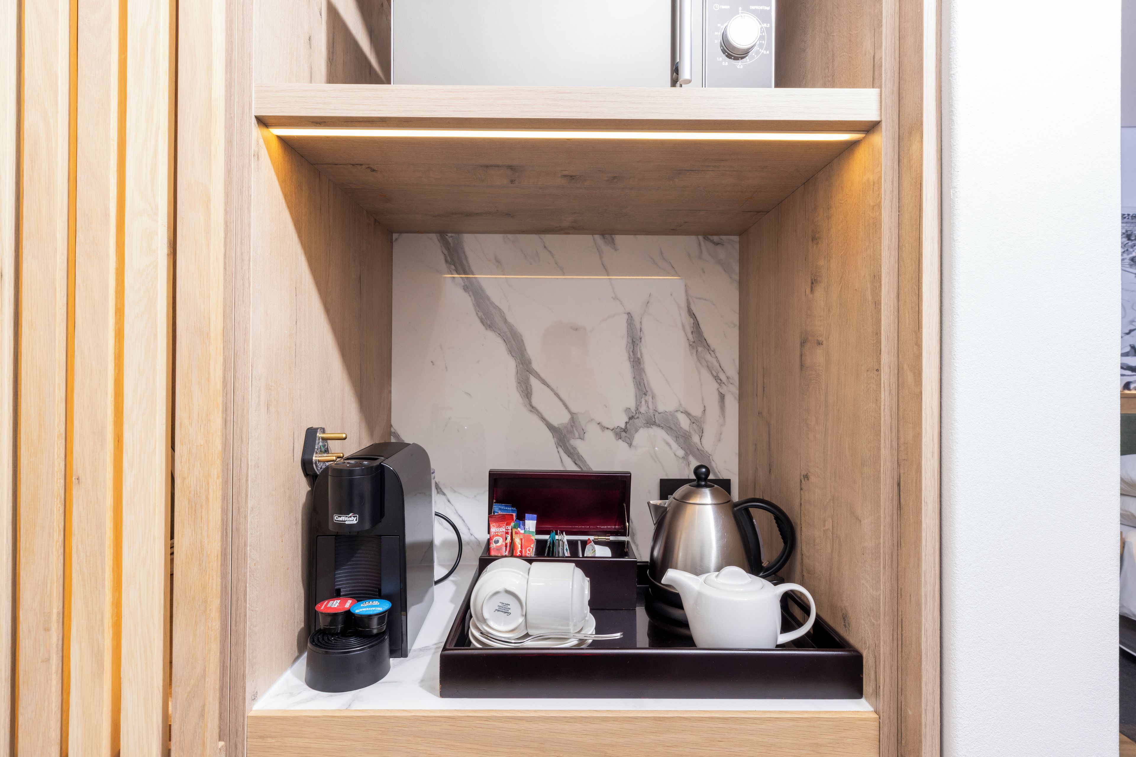 A compact kitchen area with a coffee machine, tea pot, and a cup holder.