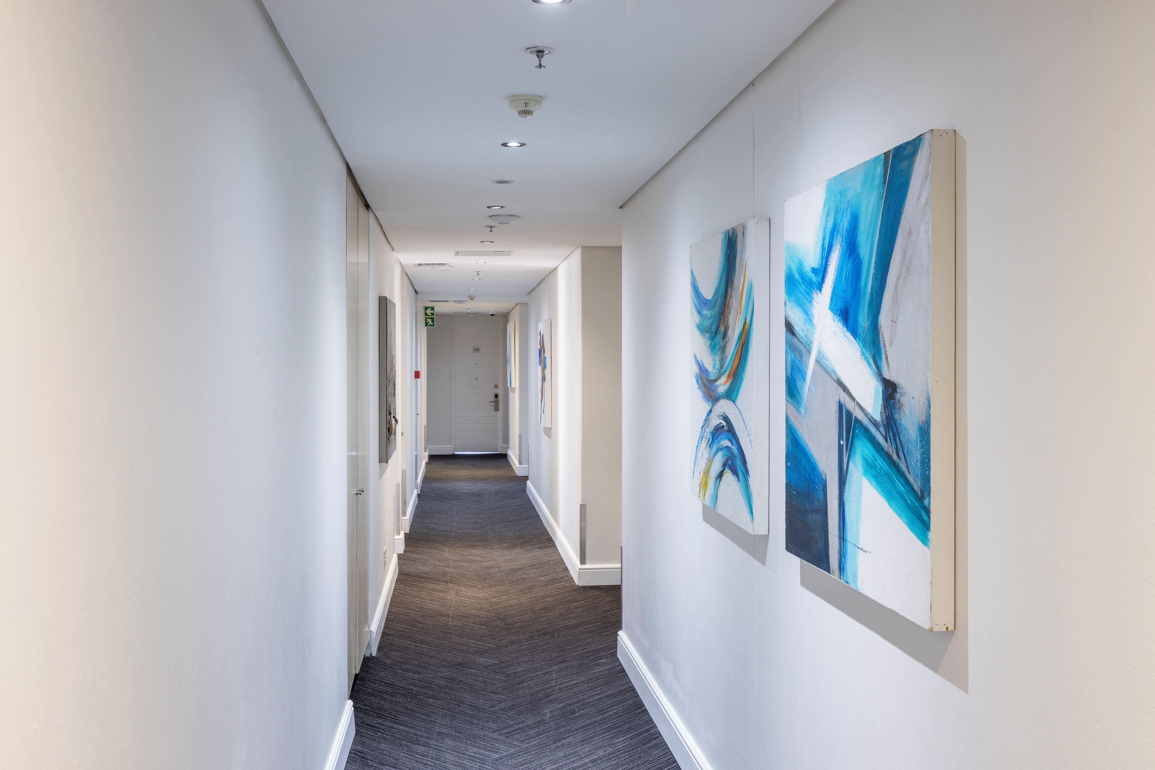 A hallway with a carpeted floor, white walls, and ceiling lights.